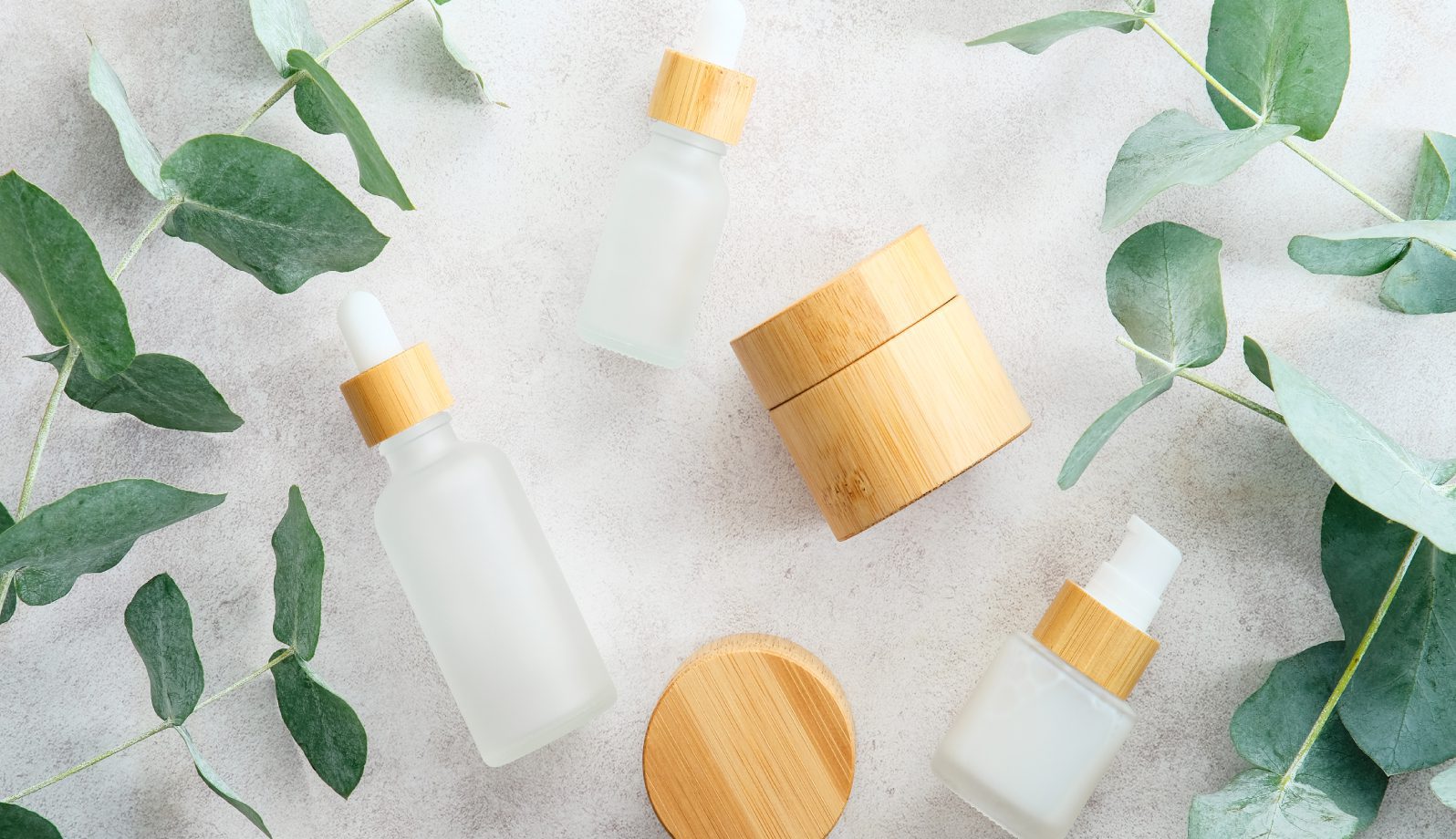 1242 Eco-friendly skincare bottles and jars with wooden lids on a soft white surface.
