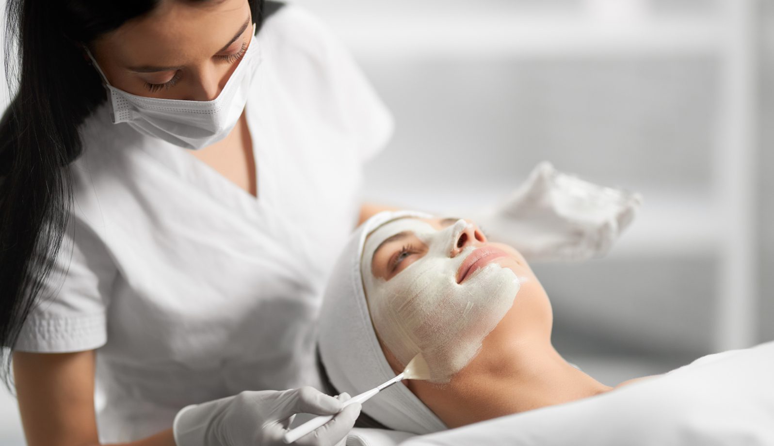 GettyImages-1170207585-13 (1) A woman receiving a facial treatment with a mask applied by a professional.