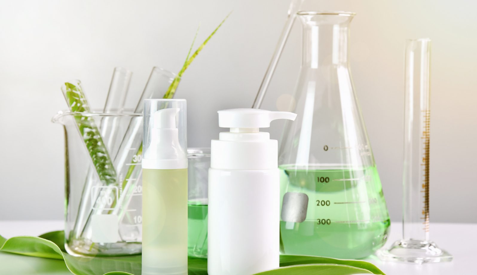 Skincare bottles and a green liquid in laboratory glassware.